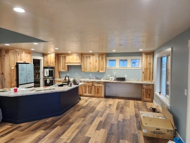 Newly renovated kitchen with wooden cabinets, blue island, light blue backsplash, and wood-look flooring.