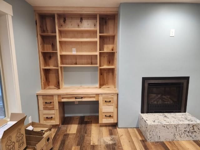 Built-in wooden desk and bookshelf unit. Blue wall and fireplace to the right. Wood floors.