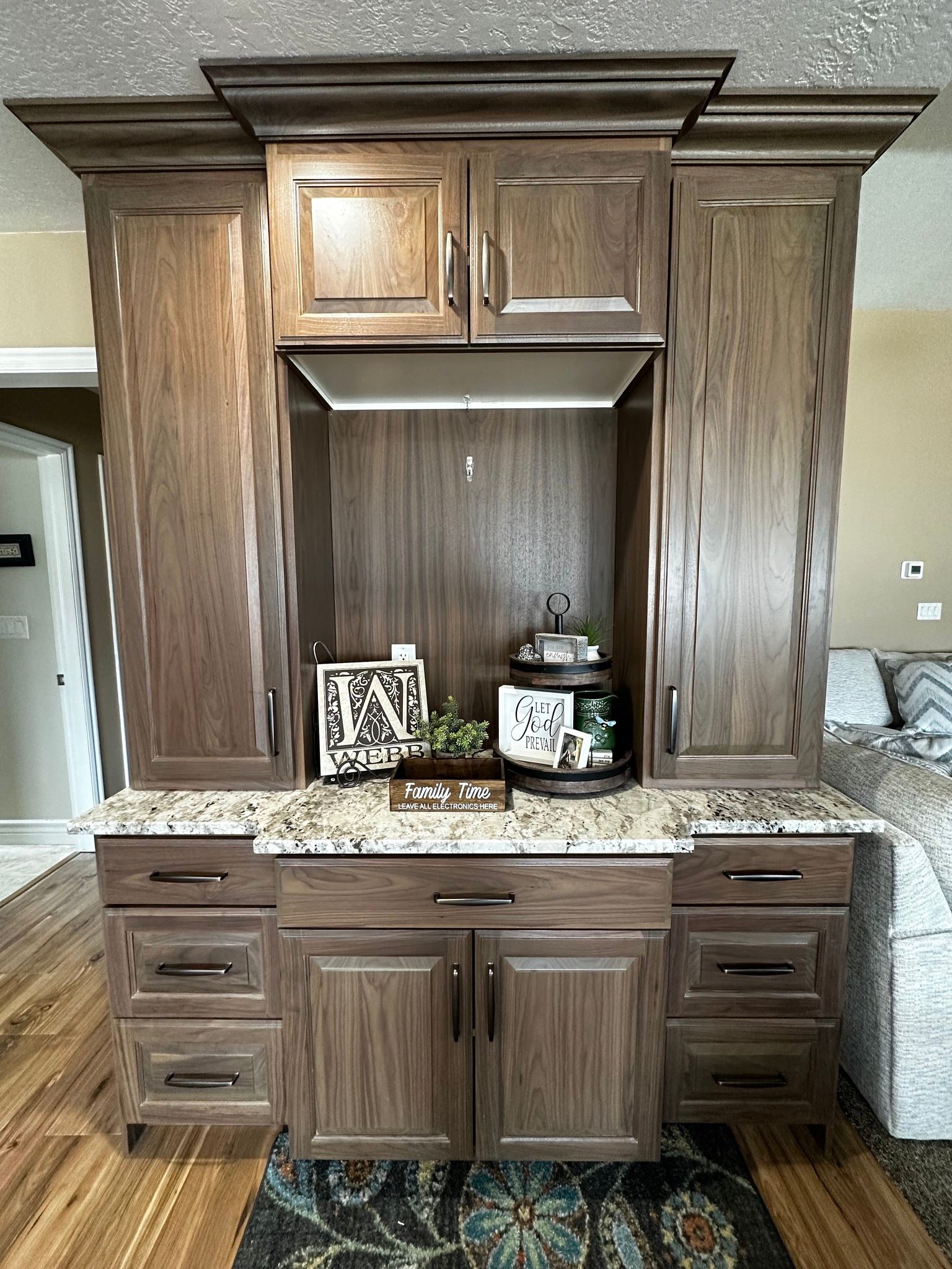Dark wood built-in cabinet with granite countertop, drawers, and upper cabinets, display niche with decor.