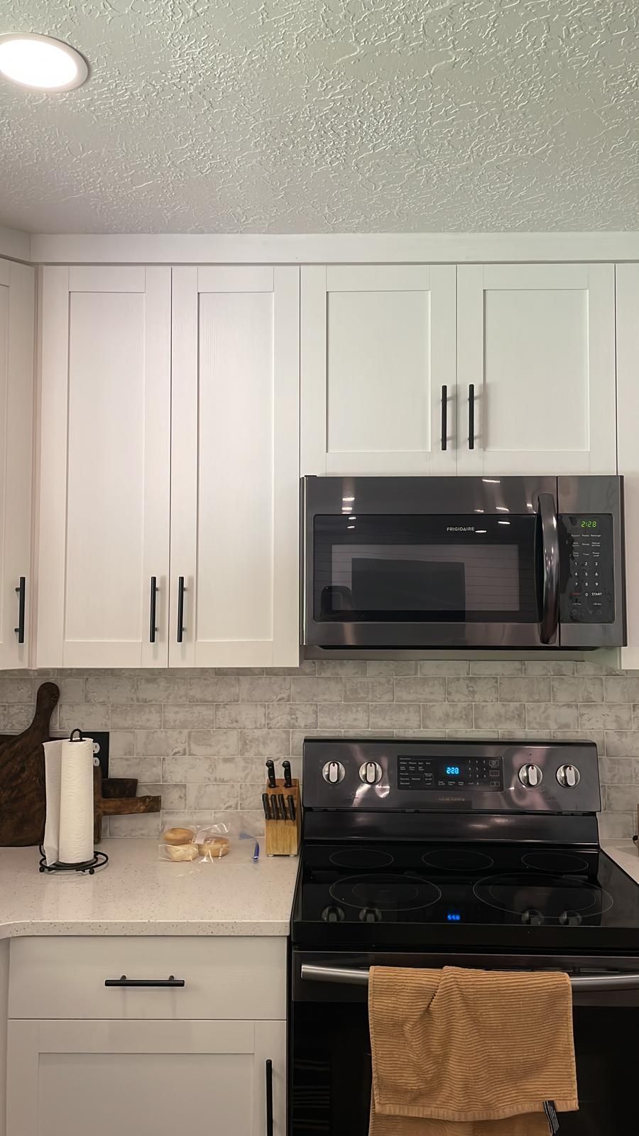 White kitchen cabinets with black handles, a stainless steel microwave and stove.