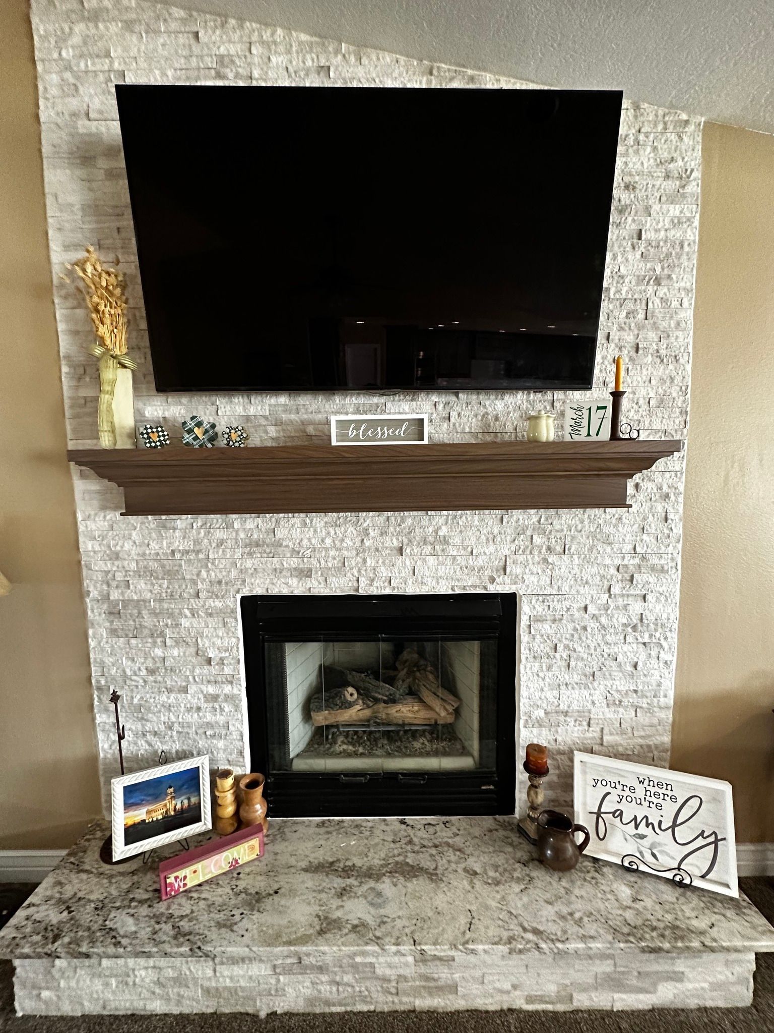 Fireplace with gray stacked stone, black TV, wooden mantel, and decorations.