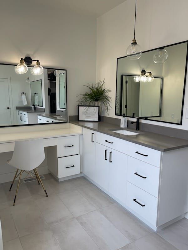 Modern white bathroom with vanity and countertop, large mirrors, black fixtures, and a potted plant.