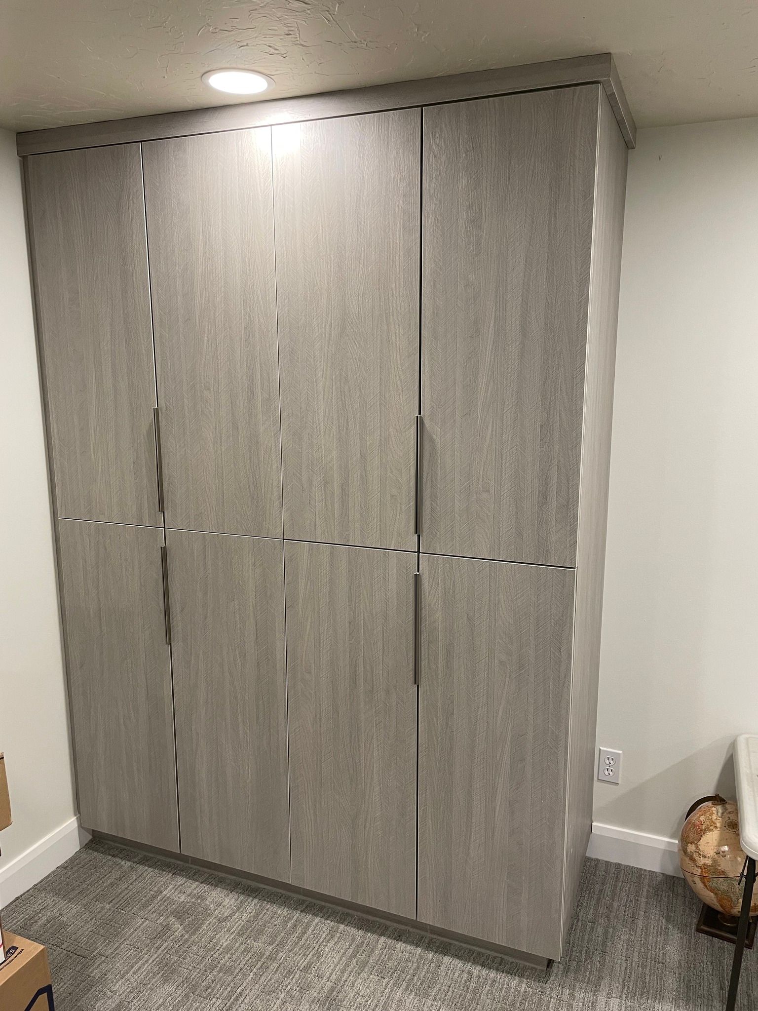 Gray built-in wardrobe with four doors in a room with carpet and a light fixture.