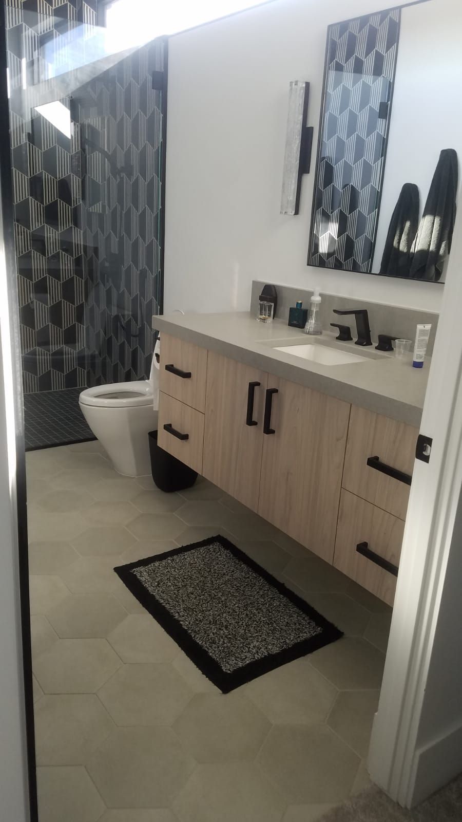 Modern bathroom with wood vanity, hexagonal floor tile, patterned accent wall, and decorative mirror.