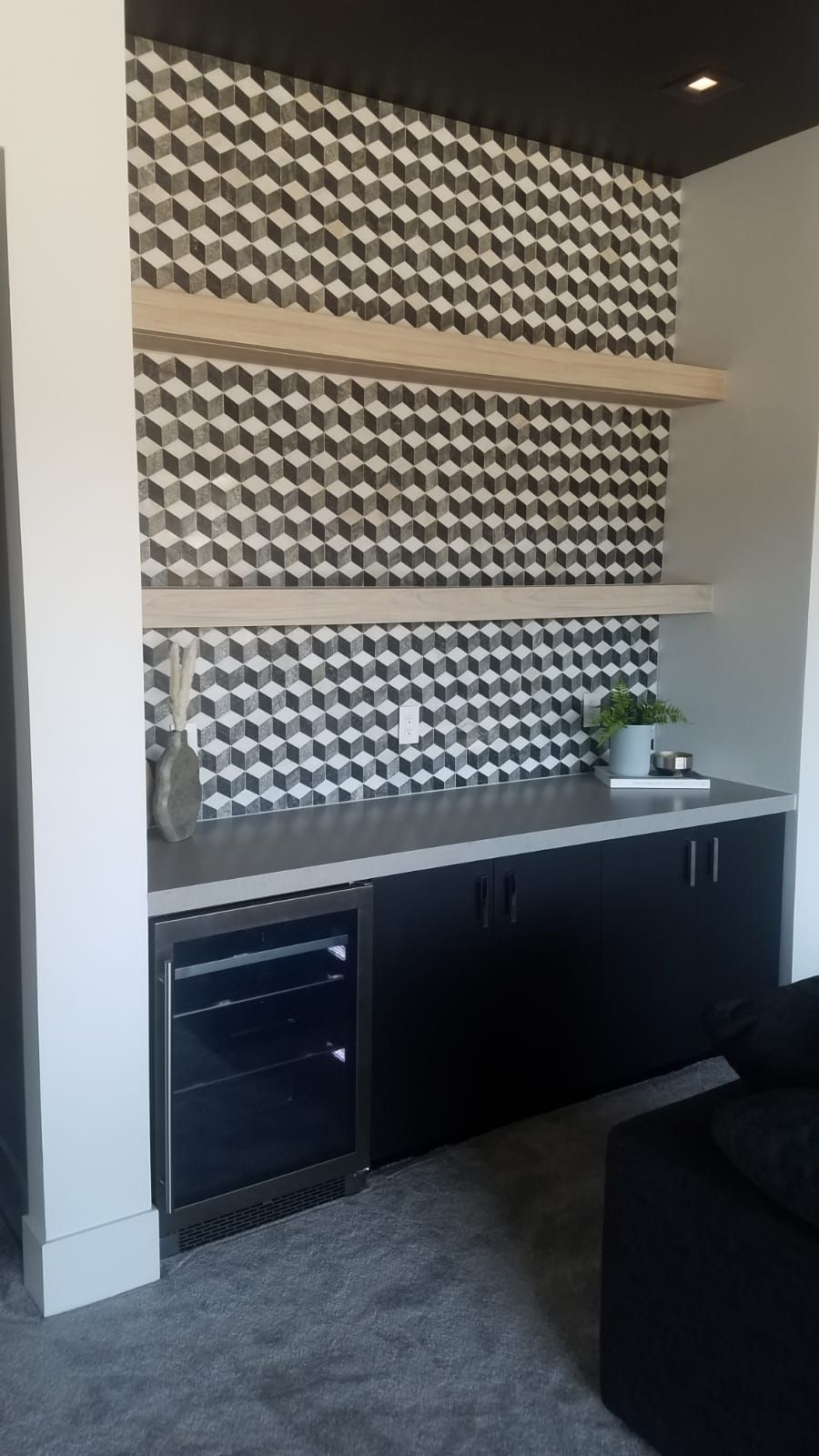 Built-in black cabinet with a beverage fridge. Wood shelves sit on a patterned wall.