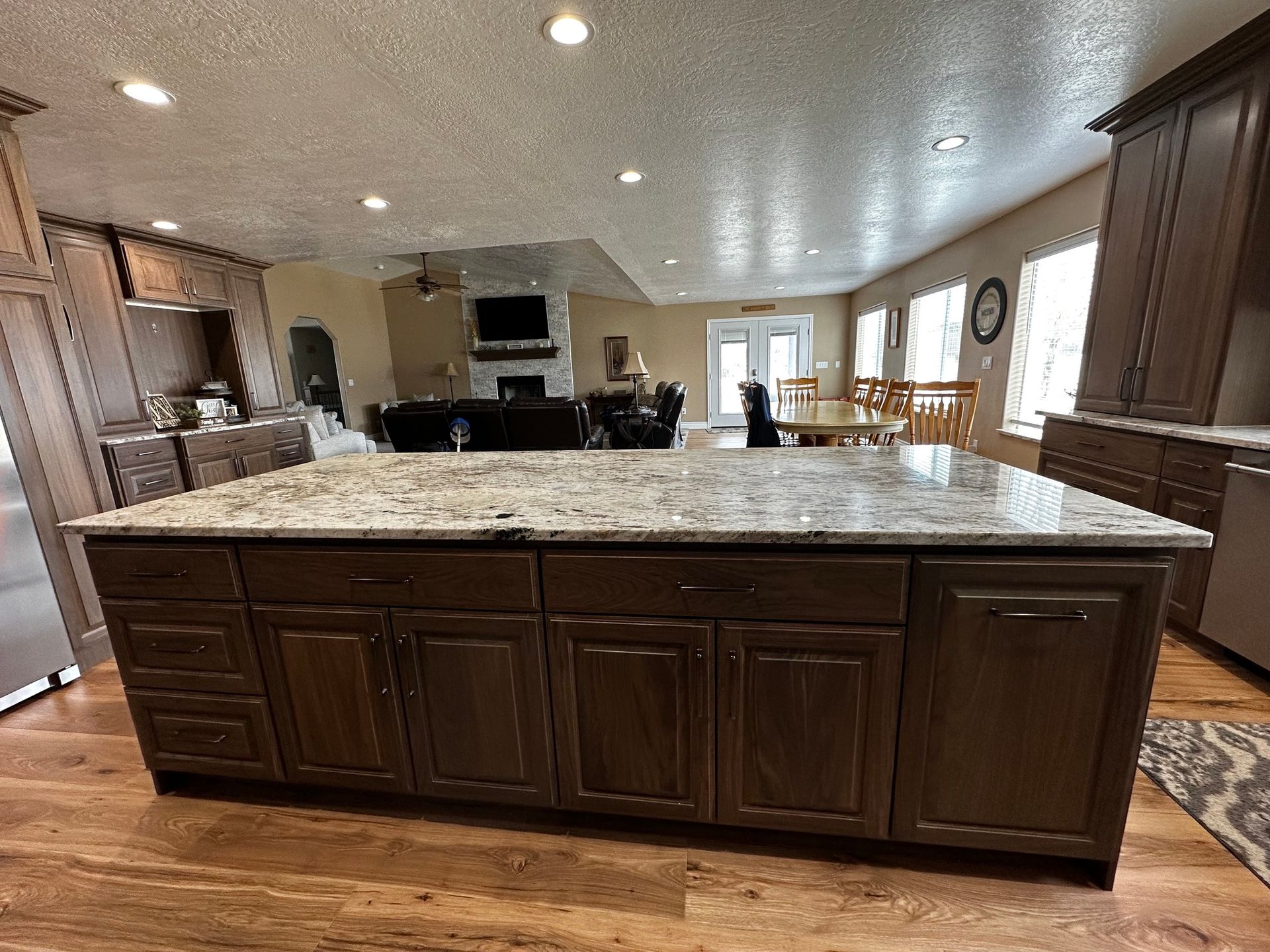 Kitchen island with granite countertop, dark brown cabinets, and wooden floors.