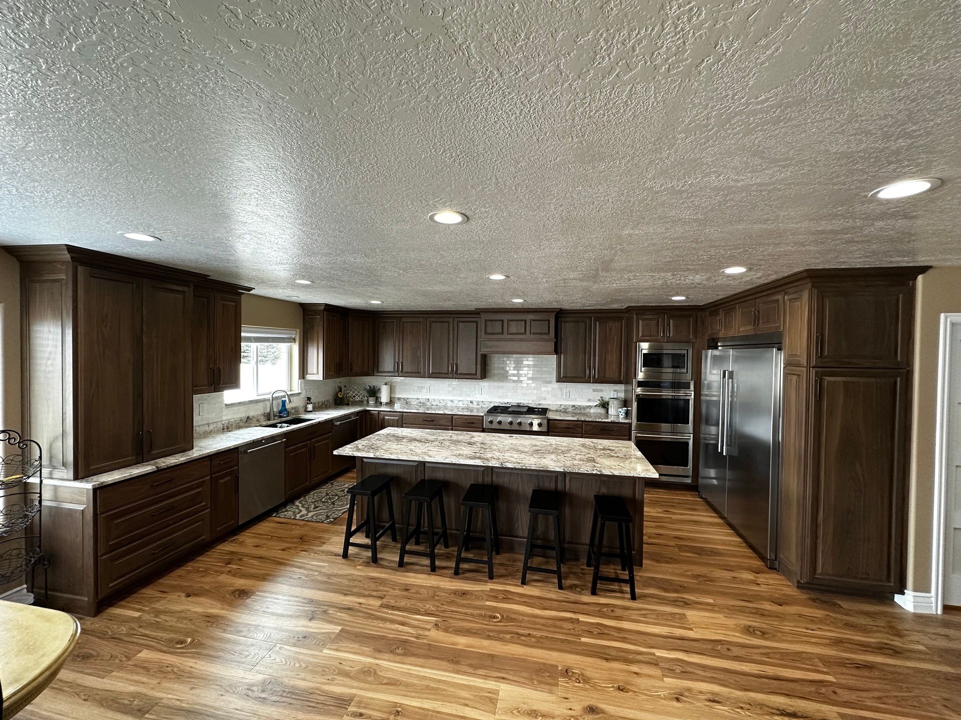 Spacious kitchen with wood cabinets, island with stools, stainless steel appliances, and wood floor.