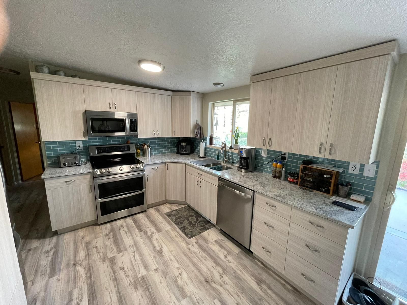 Kitchen with light wood cabinets, stainless steel appliances, and blue tile backsplash.