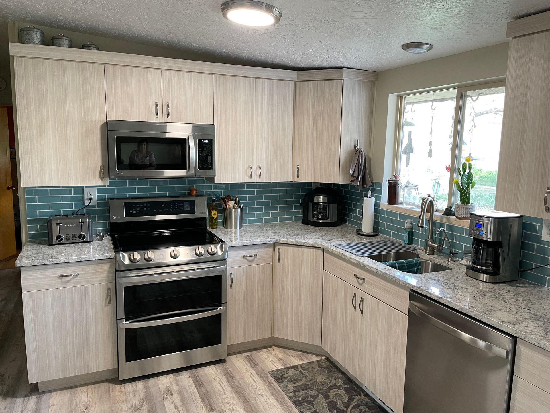 Kitchen with light wood cabinets, stainless steel appliances, and turquoise tile backsplash.