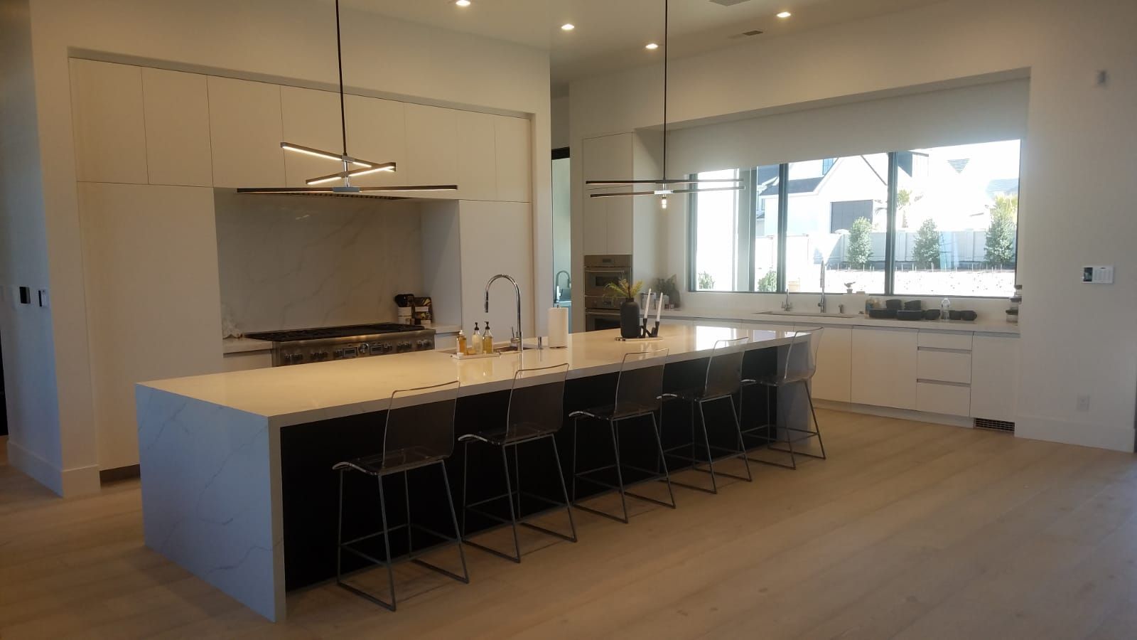 Modern kitchen with large island, seating, white countertops, dark cabinets, and pendant lights.