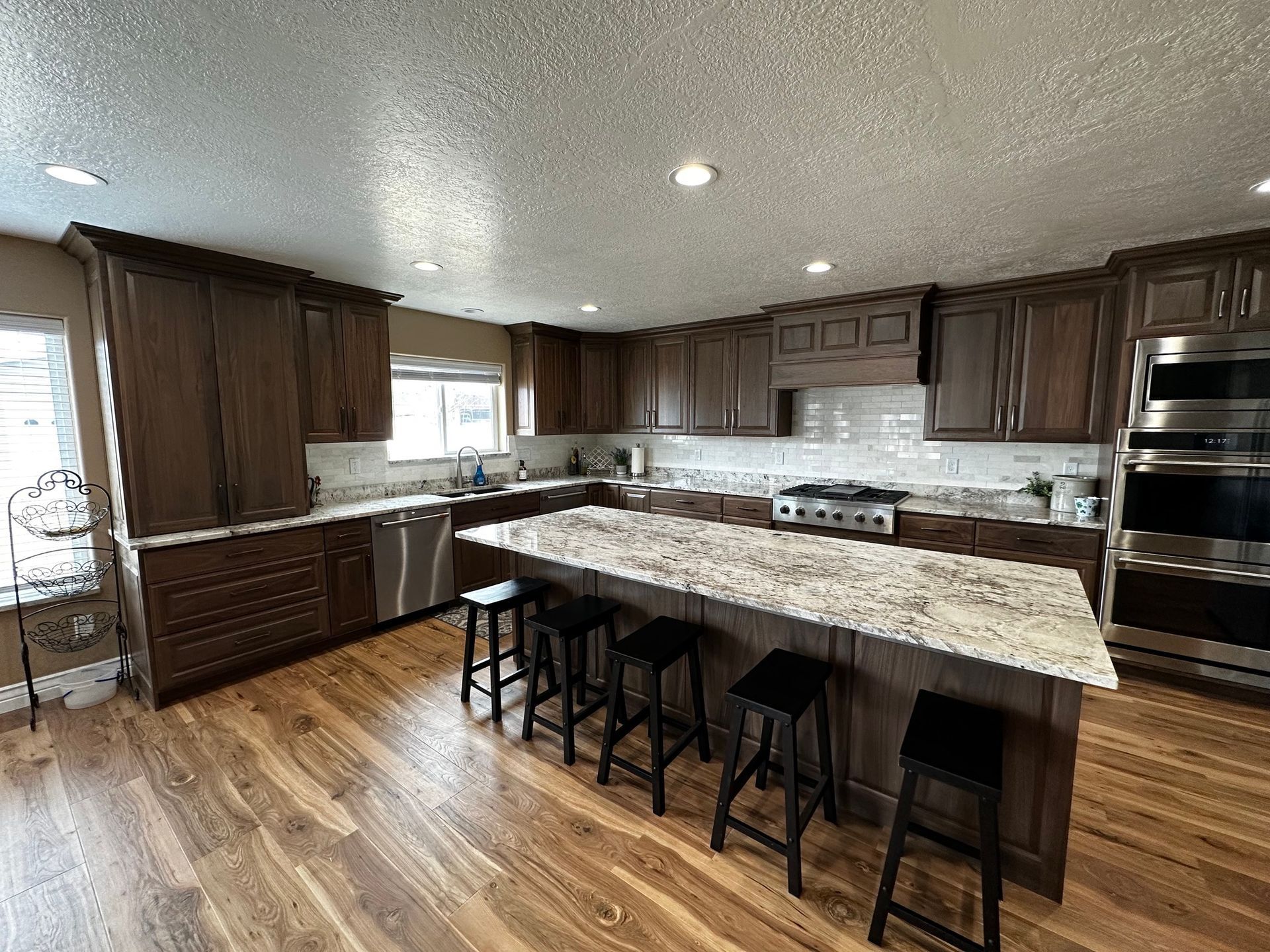 Kitchen with dark brown cabinets, granite countertops, island with seating, and stainless steel appliances.