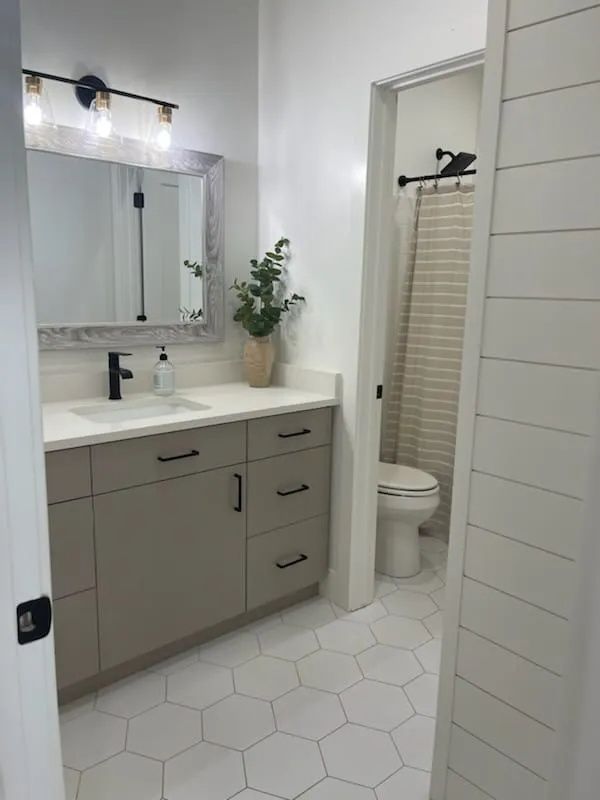 Modern bathroom with grey vanity, white countertops, and hexagon tile floor.