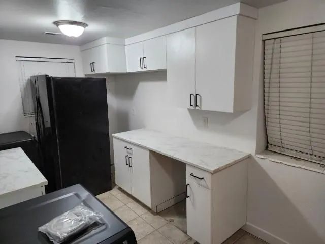 White kitchen cabinets with black handles, a white countertop, and a black refrigerator.