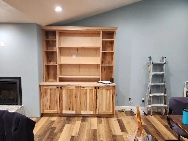 Wooden built-in cabinet with shelves and closed door storage against a blue wall; a ladder and chair are nearby.