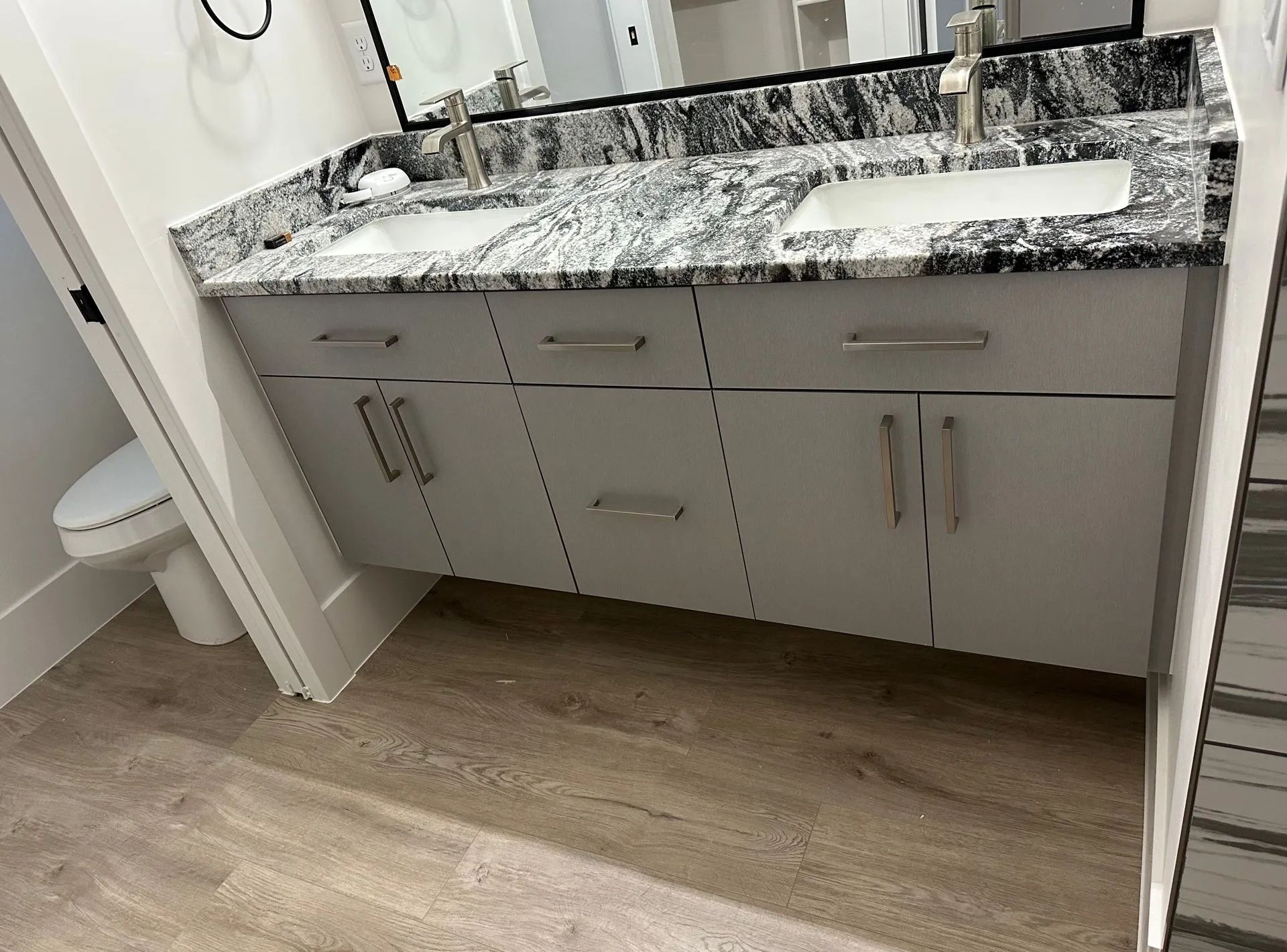 Modern bathroom vanity with double sinks, light gray cabinets, and granite countertop.