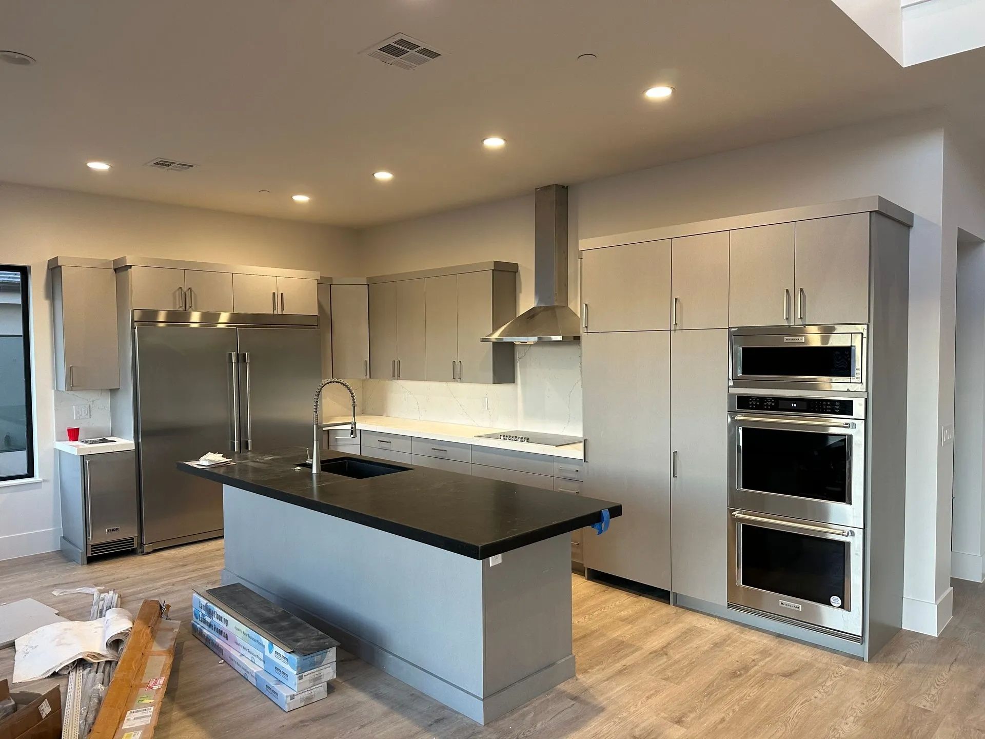 Modern kitchen with gray cabinets, stainless steel appliances, and black island countertop.