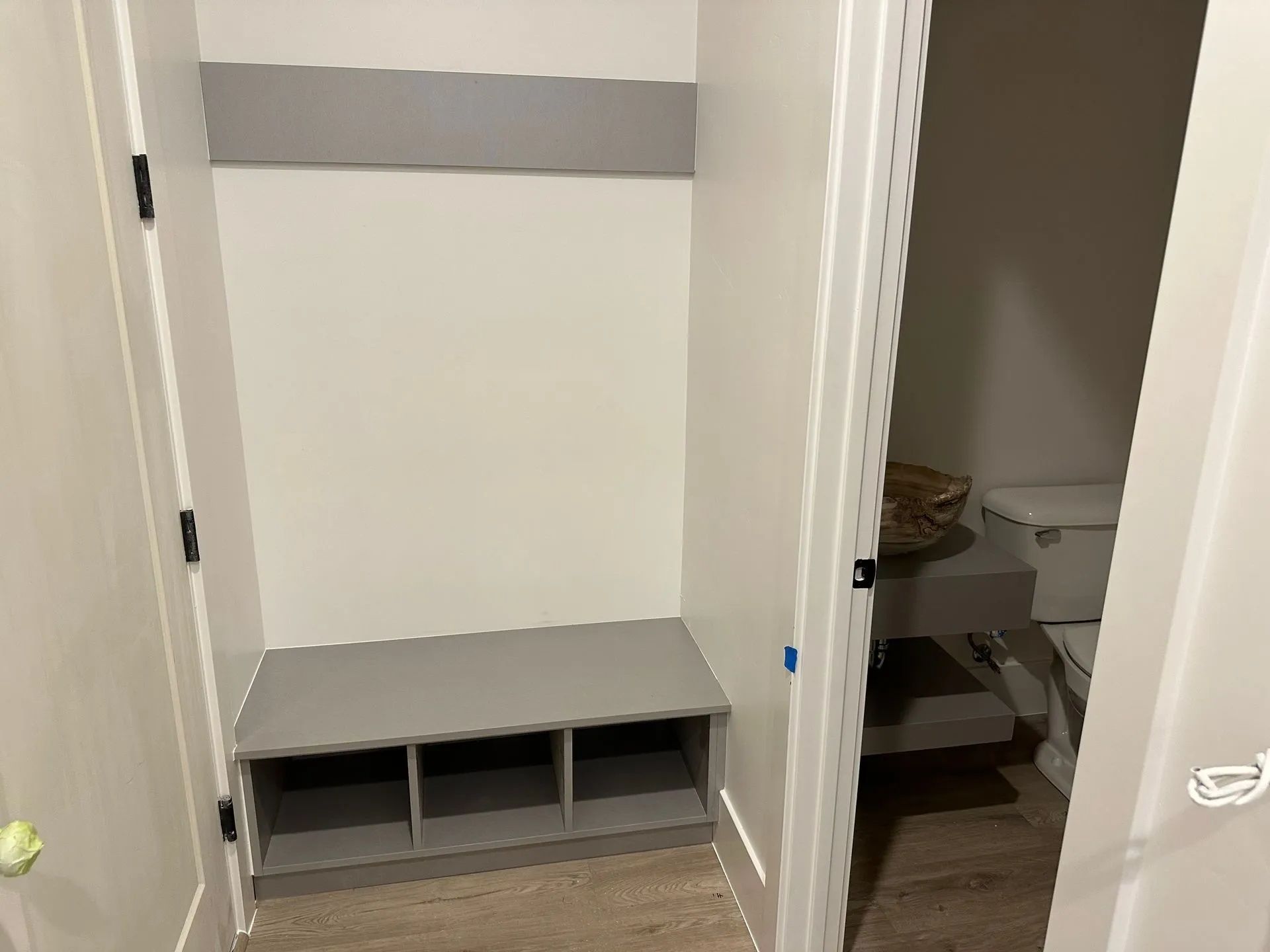 Entryway with built-in bench and shoe cubbies, painted gray, with an open door to a toilet.