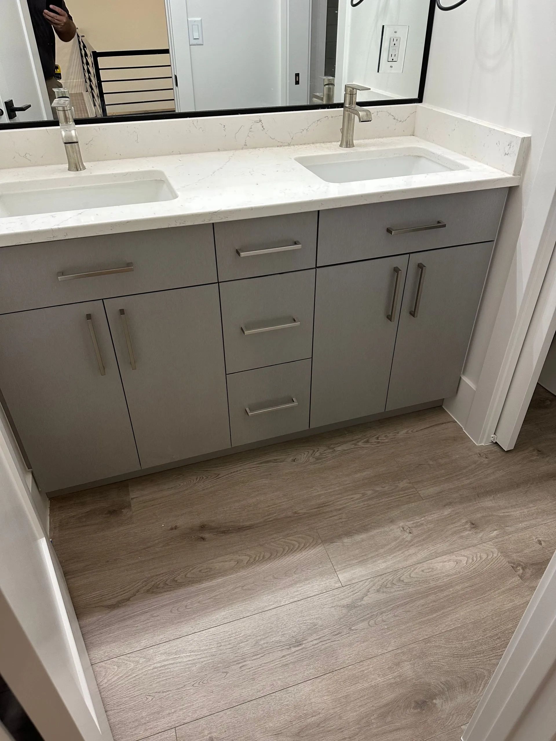 Bathroom with gray vanity, two sinks, white countertop, and light wood-look flooring.