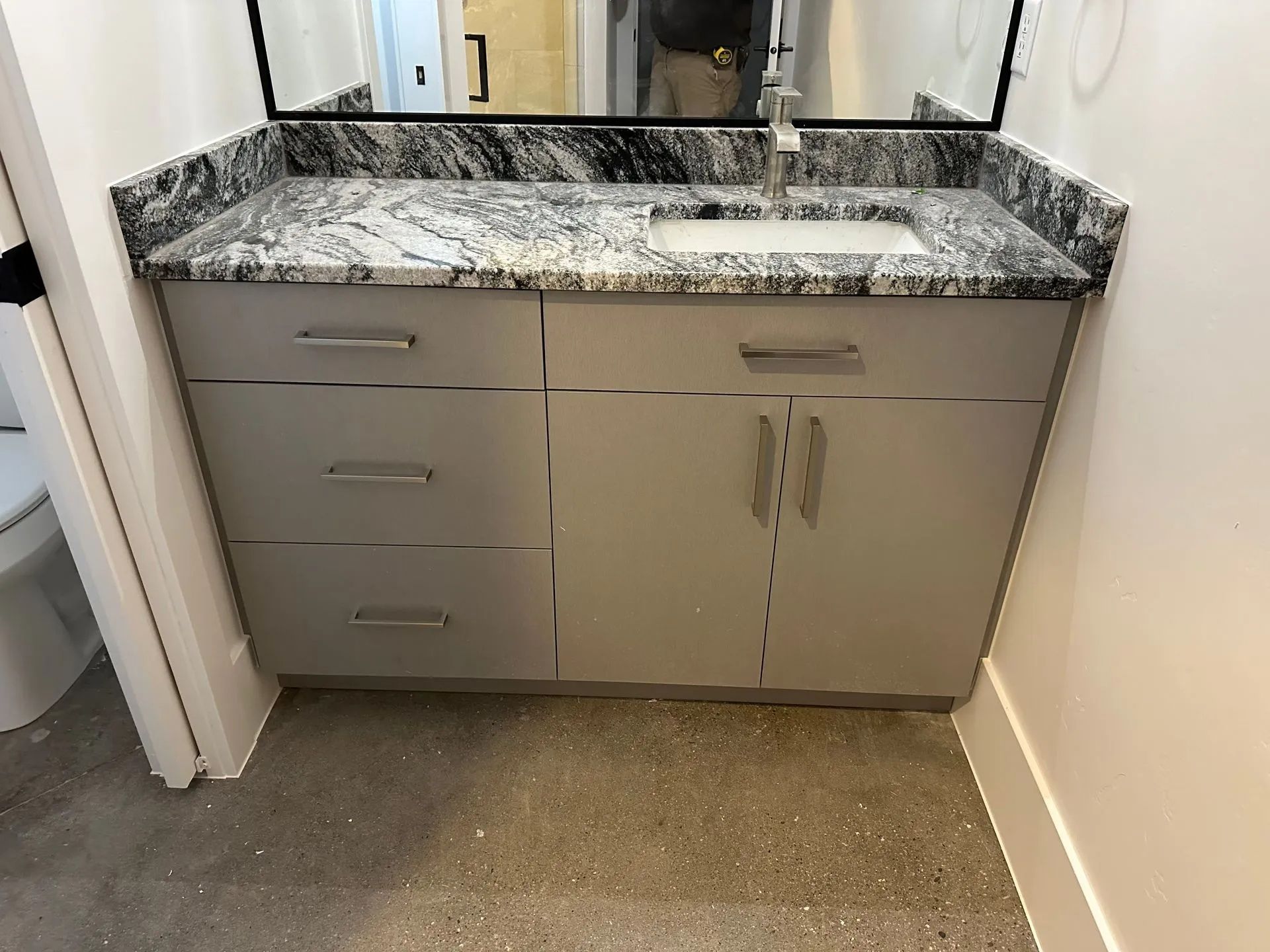Bathroom vanity with gray cabinets, granite countertop, and rectangular mirror.