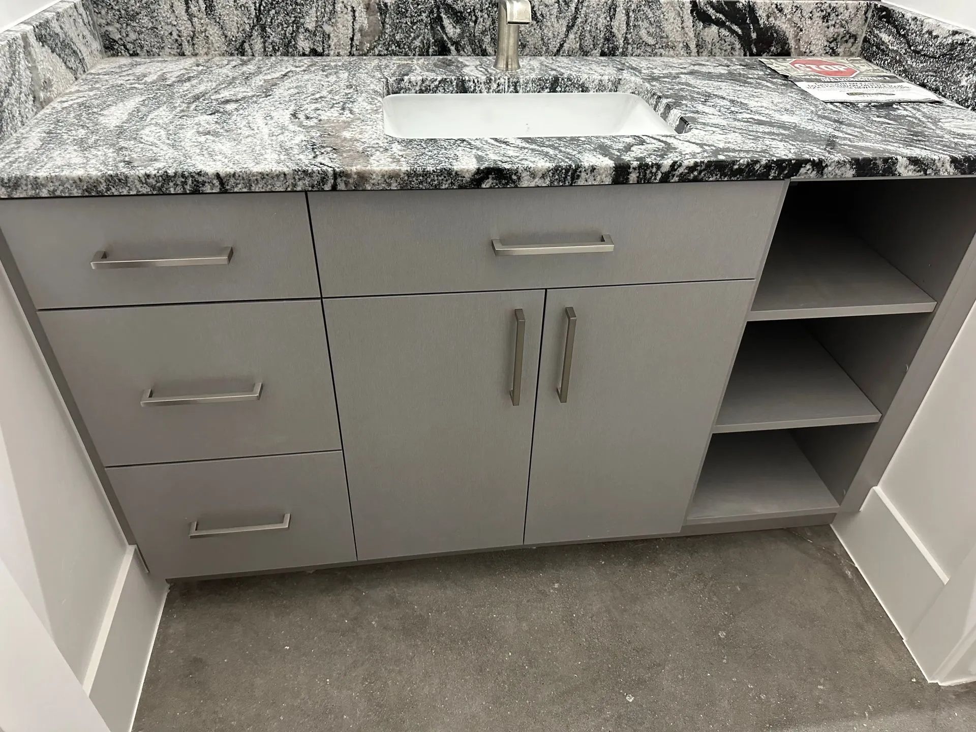 Gray bathroom vanity with granite countertop, sink, and storage shelves.