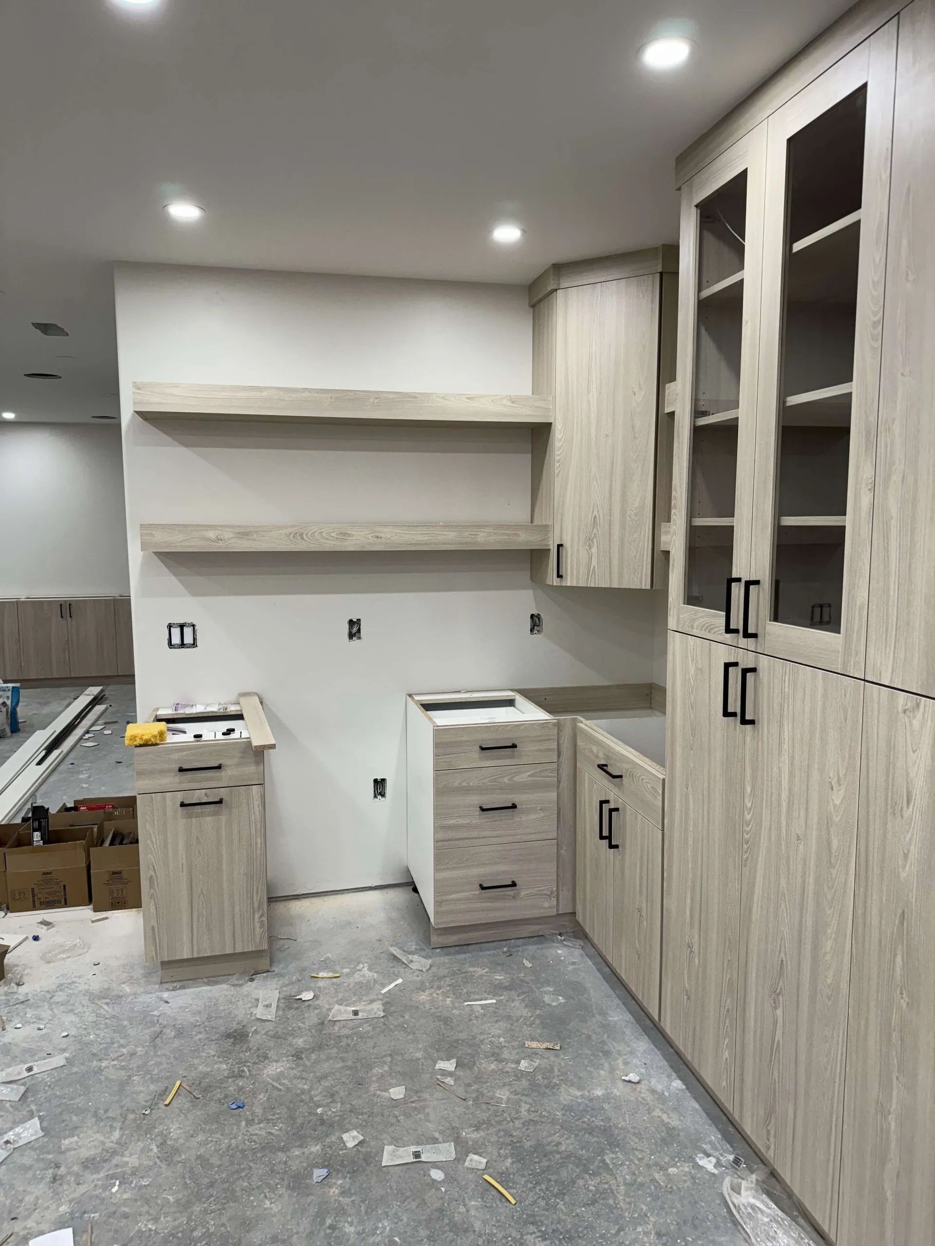 Kitchen under construction with light wood cabinets and shelves.