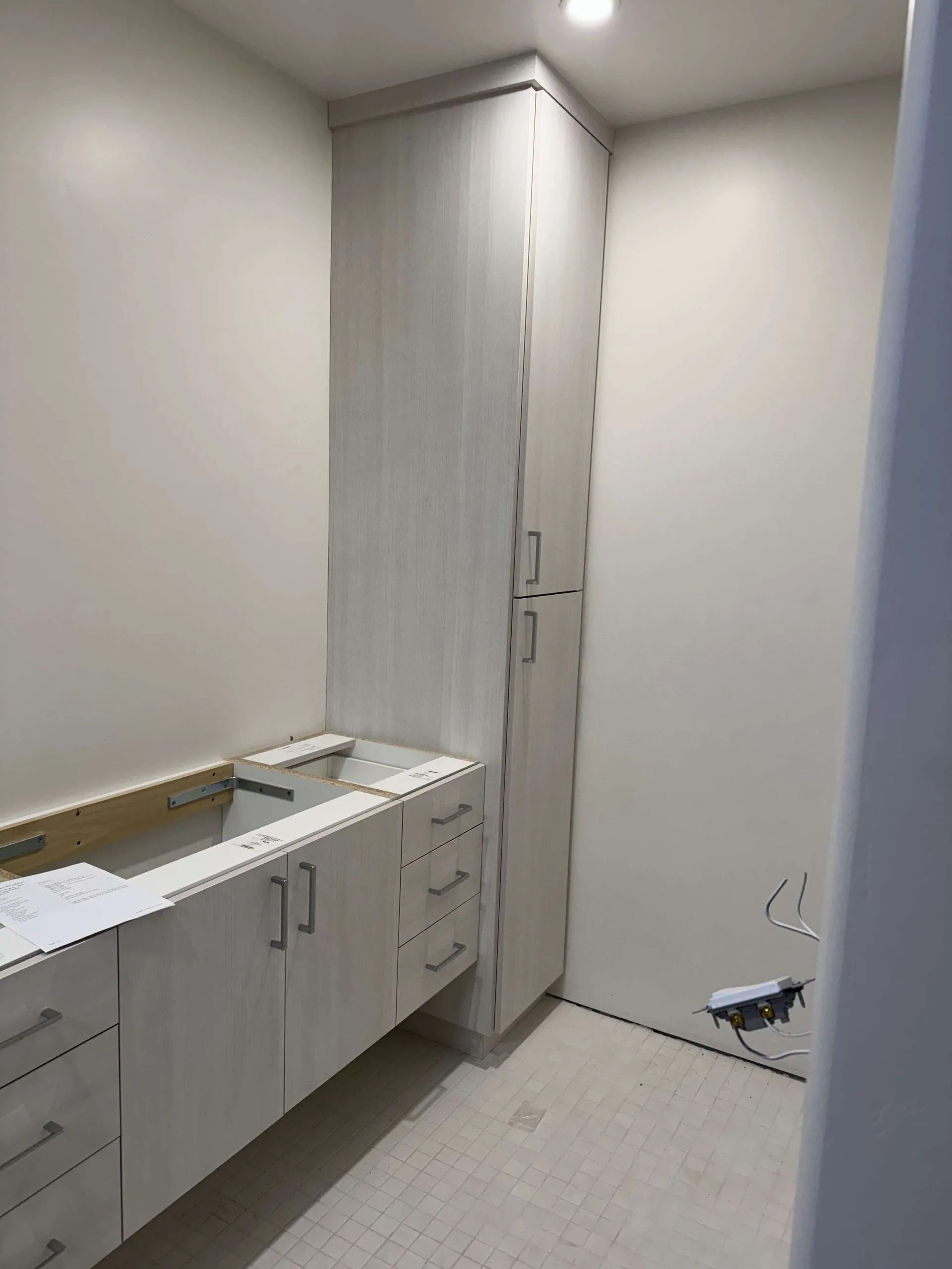 Bathroom under construction with a vanity, tall cabinet, and light-colored walls.