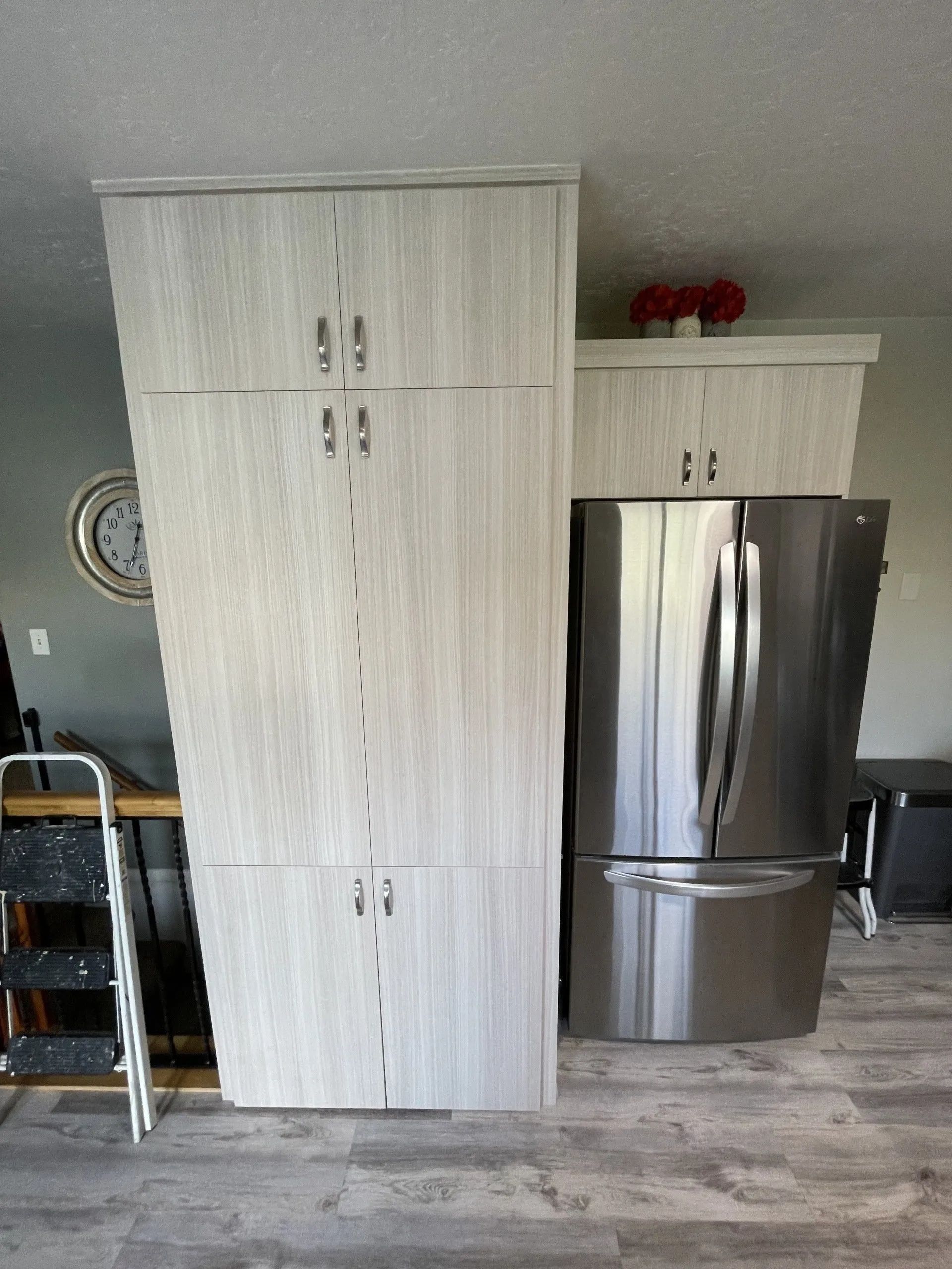 Tall, light-colored kitchen cabinets beside a stainless steel refrigerator. A small ladder is to the left.