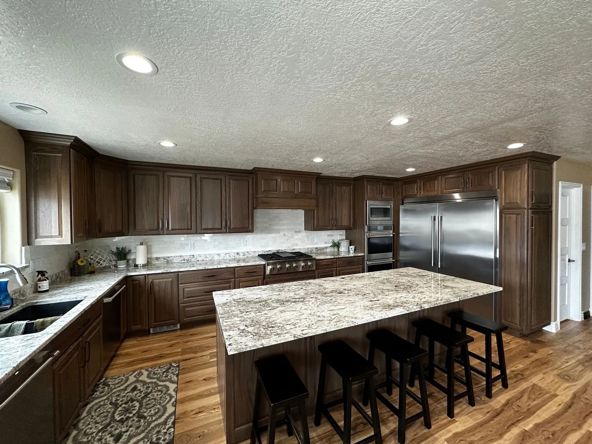 Spacious kitchen with dark wood cabinets, granite countertops, and a large island with stools.