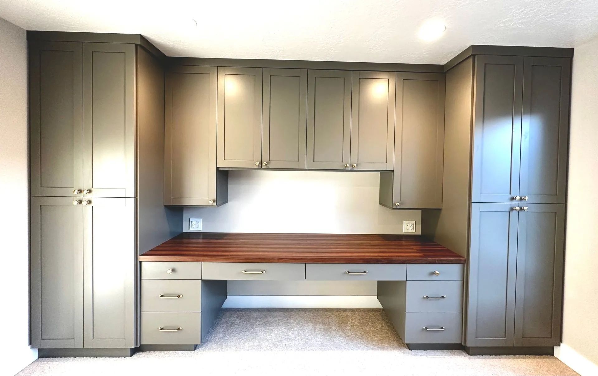 Built-in home office with gray cabinets, a wooden desk, and overhead storage.