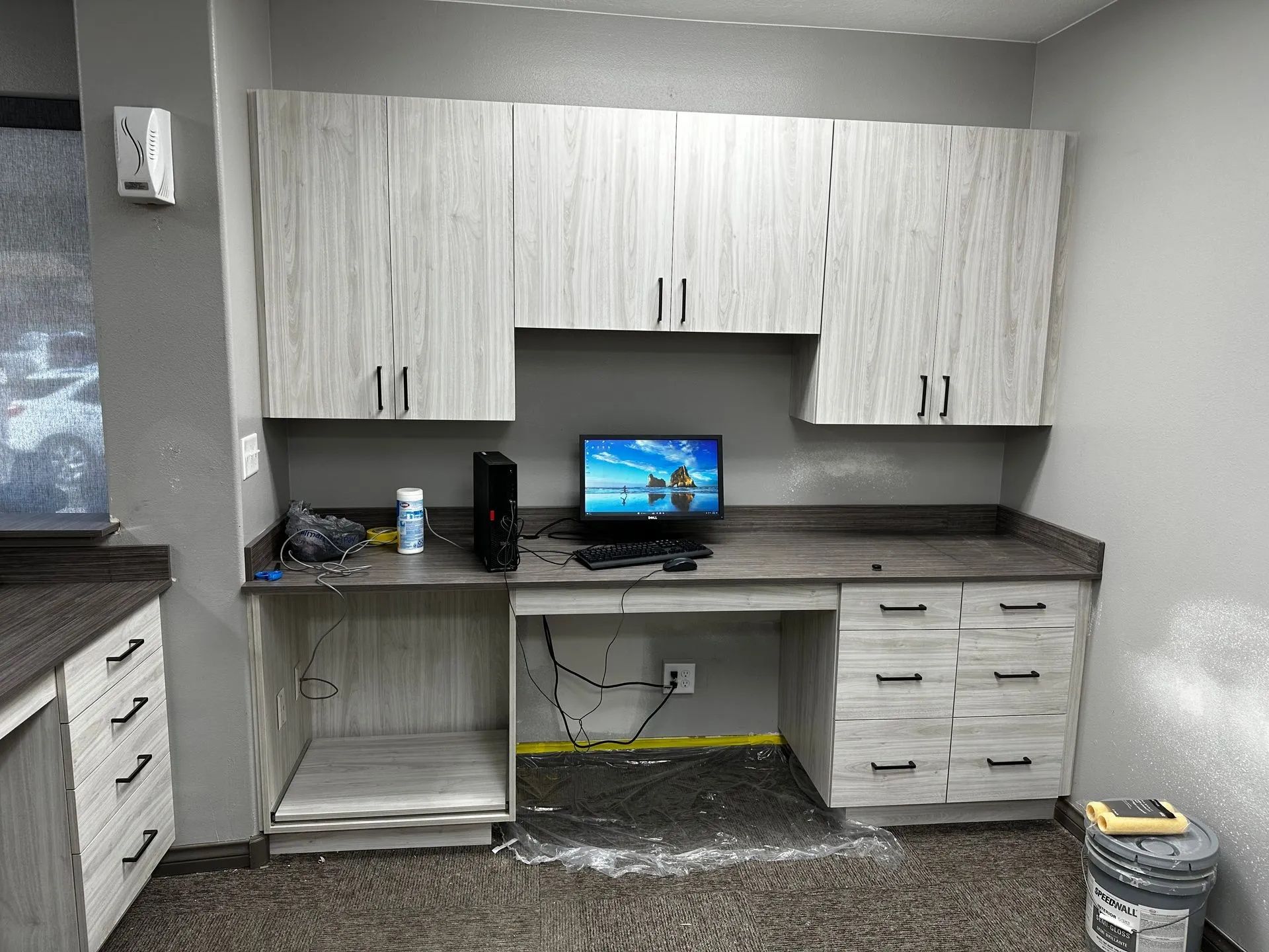 Office desk with cabinets and computer. Gray cabinets, countertop, and walls.