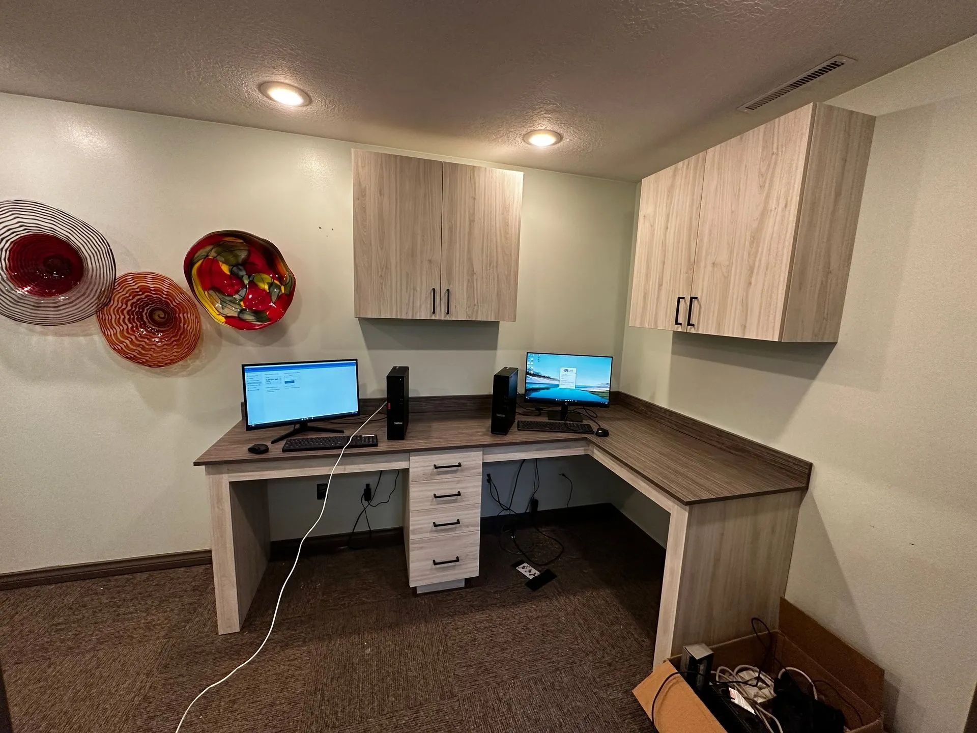 Corner desk with two computers, two cabinets, and decorative wall art.