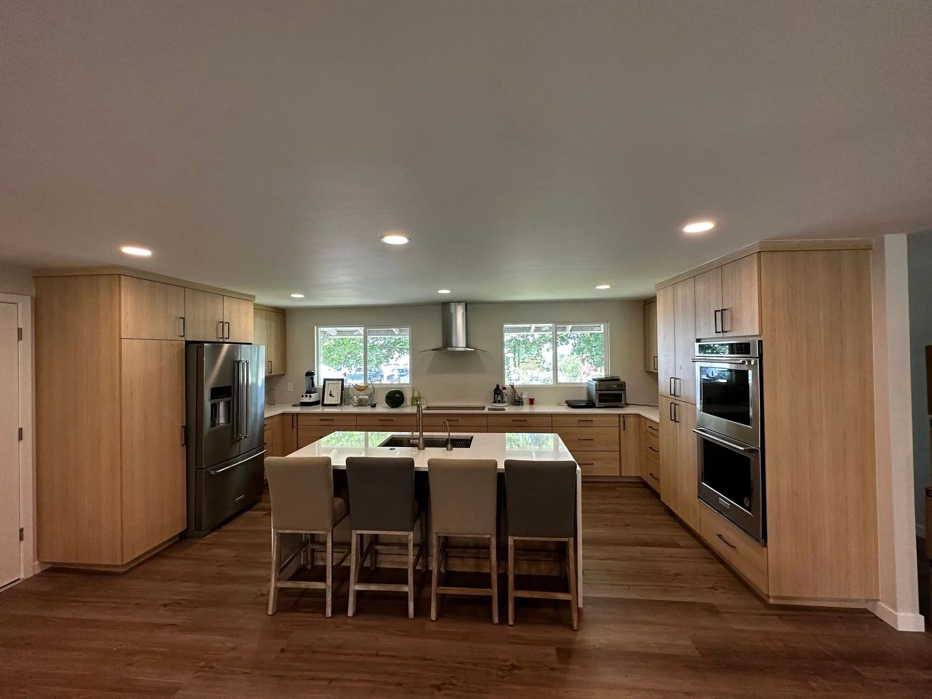 Modern kitchen with light wood cabinets, a large island with chairs, and stainless steel appliances.