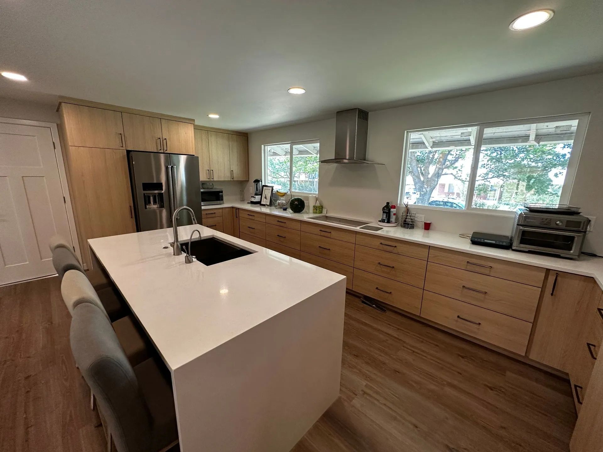 Modern kitchen with light wood cabinets, white countertops, and an island with a sink.