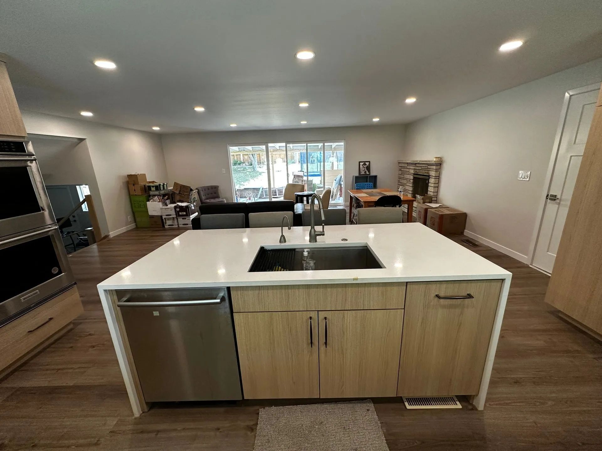 Modern kitchen with island, sink, and dishwasher. Open to living room with seating, fireplace, and window.