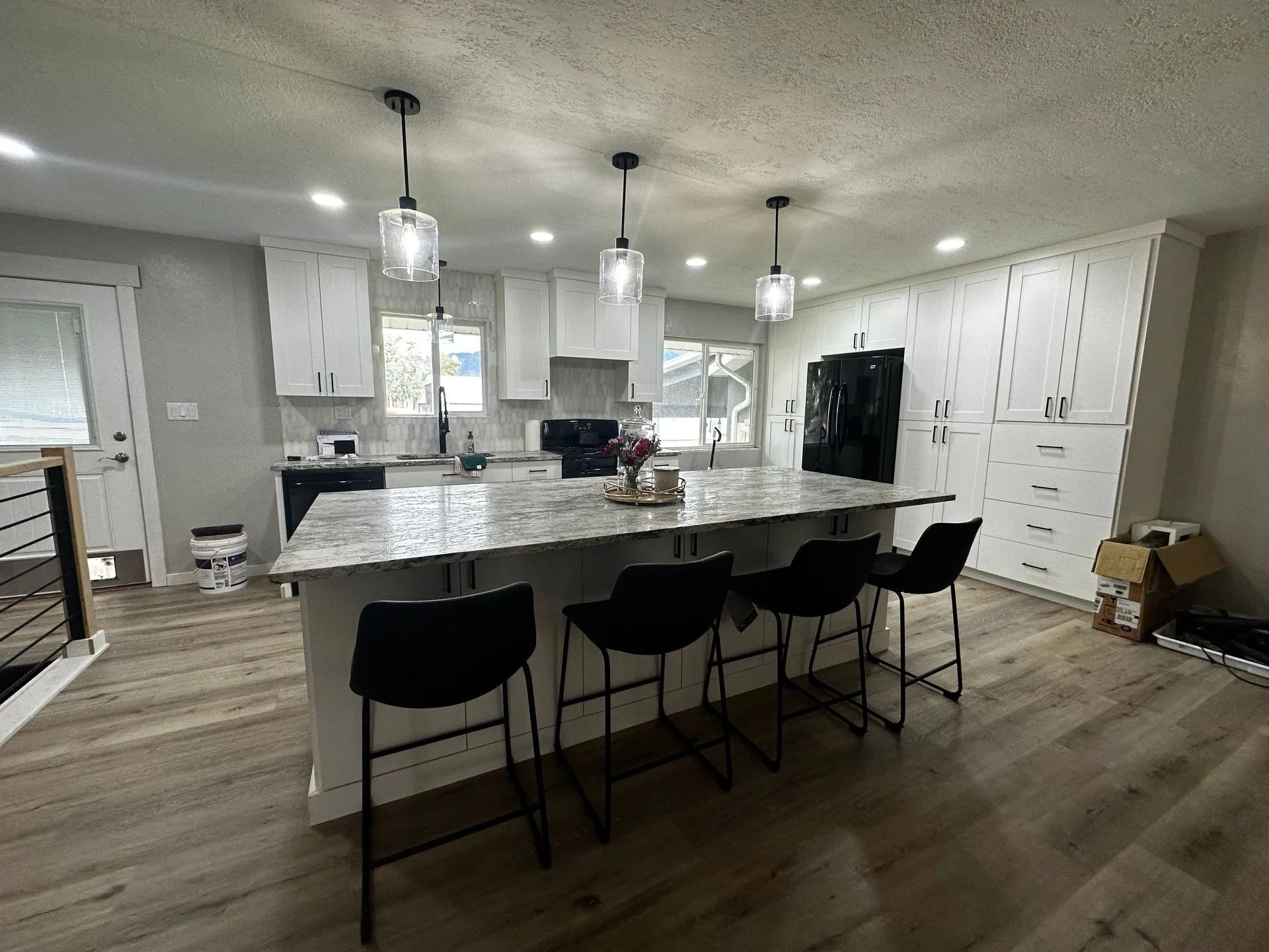 Modern kitchen with white cabinets, large island with seating, pendant lights, and black appliances.