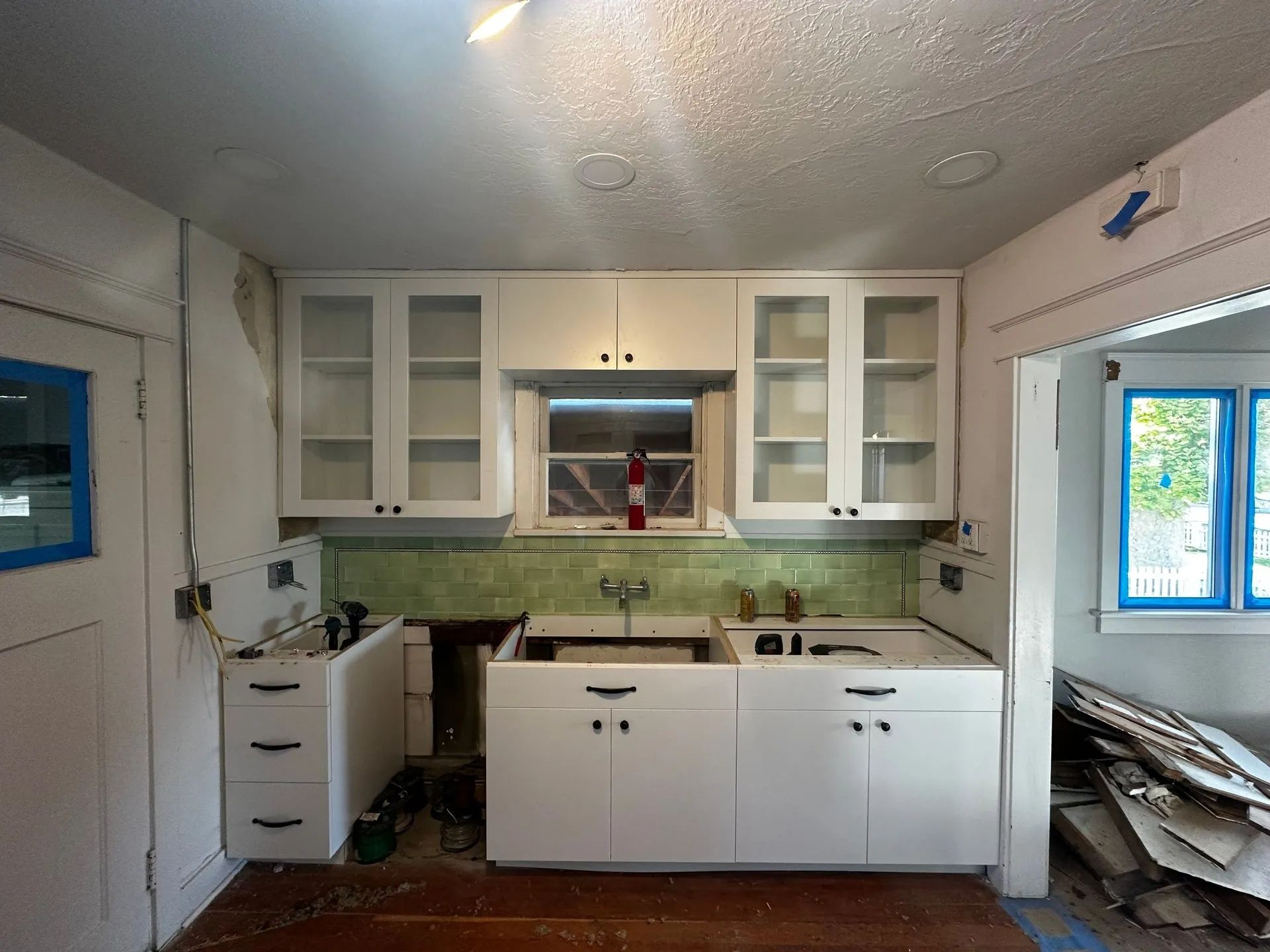 Kitchen under renovation with white cabinets, green backsplash, and a window.