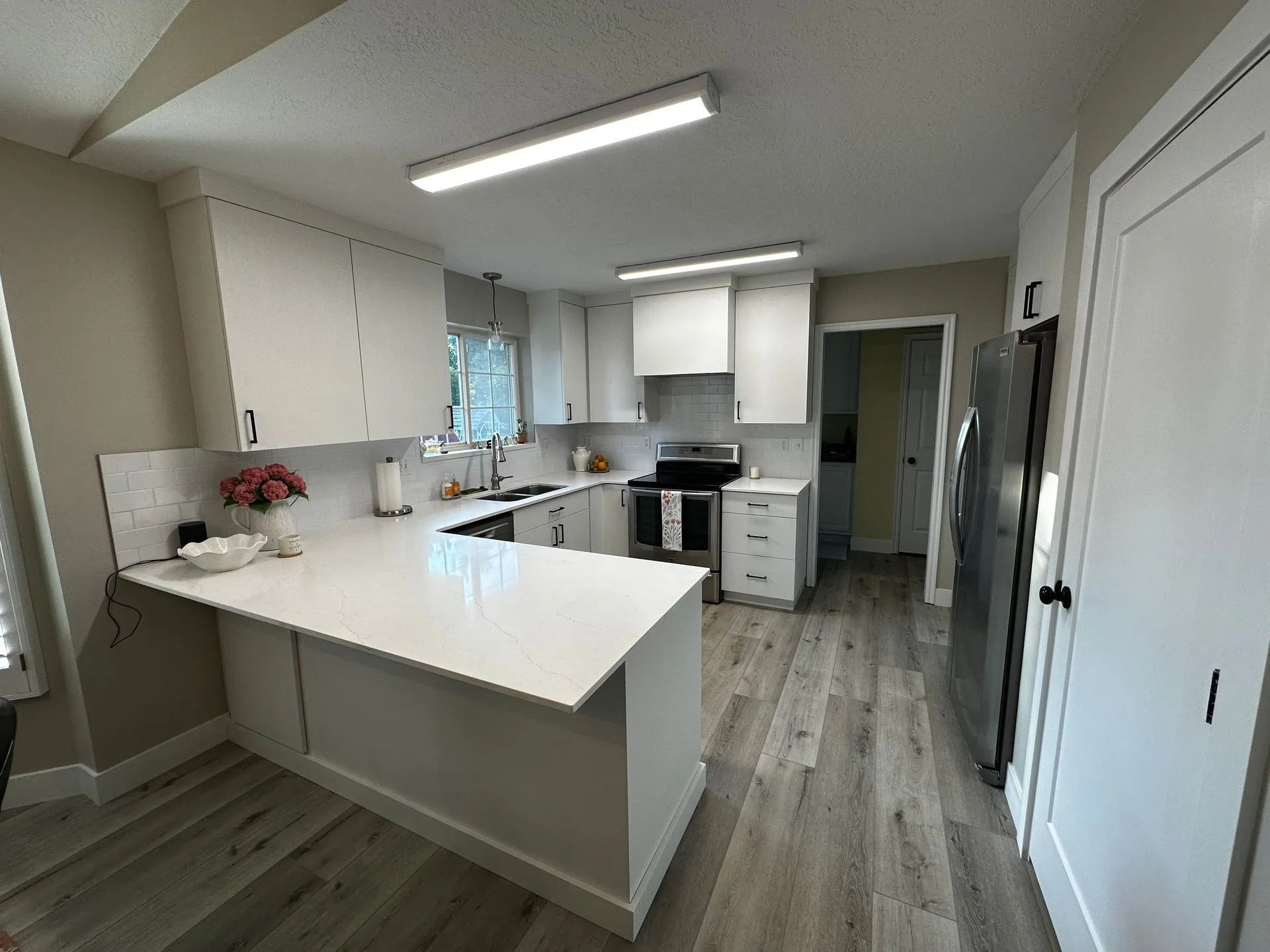 Bright, modern kitchen with white cabinets, light countertops, and gray wood-look flooring.
