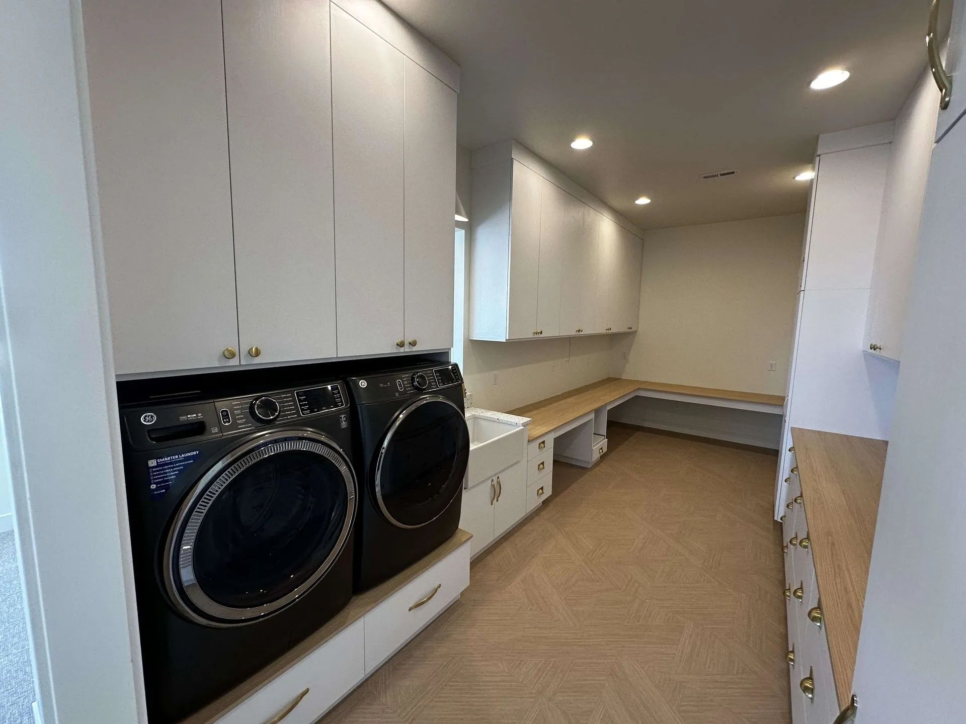 Laundry room with white cabinets, dark washer and dryer, and a wooden countertop.