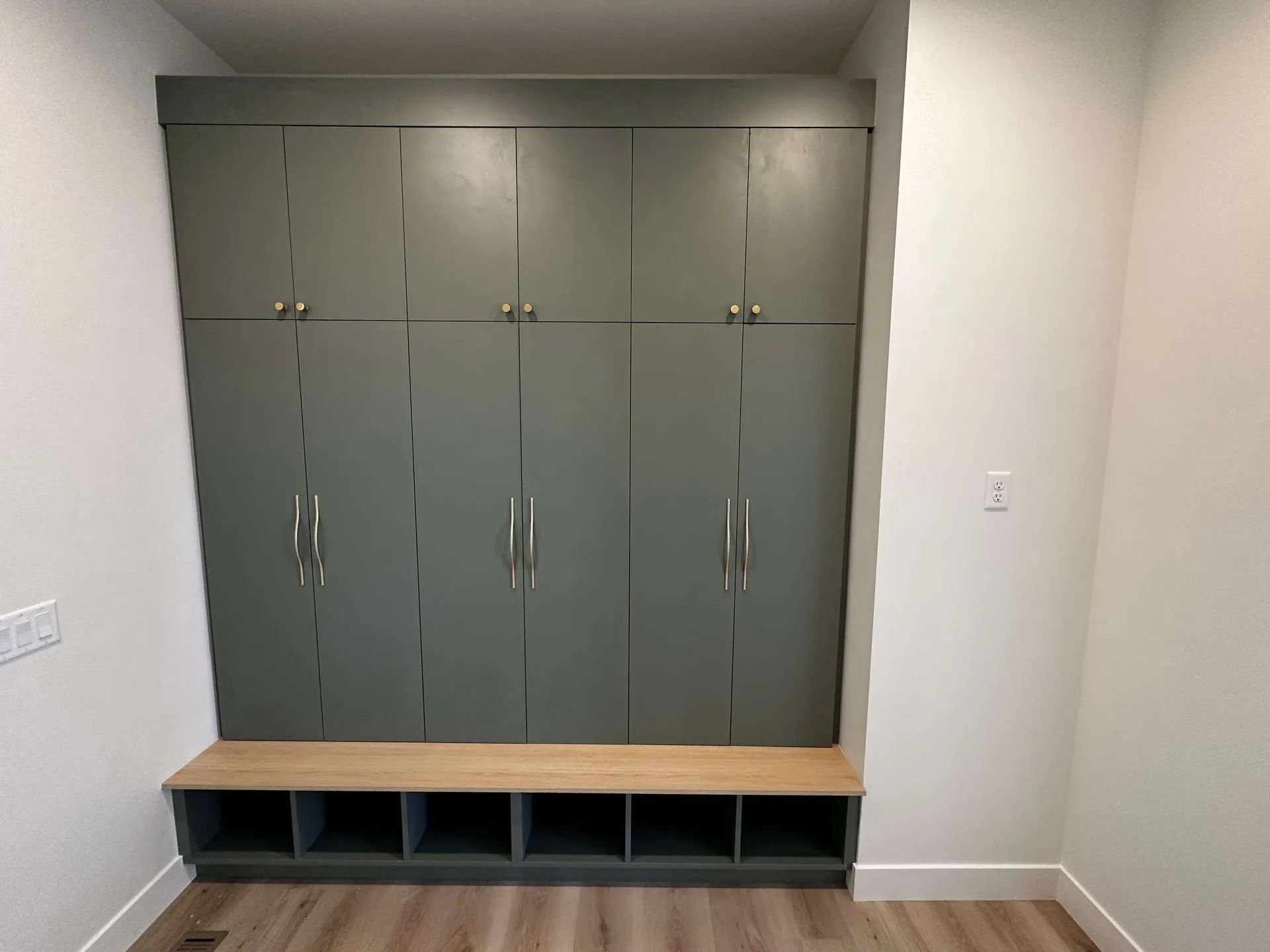 Built-in storage unit with cabinets and a bench in a room with light-colored walls and wood-look flooring.