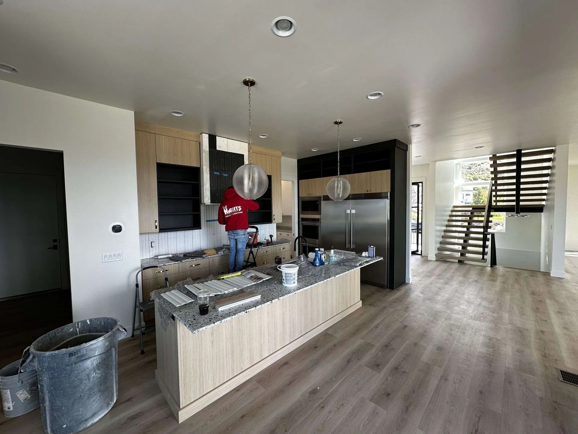 Person installing cabinets in a modern kitchen with island and stainless steel appliances.