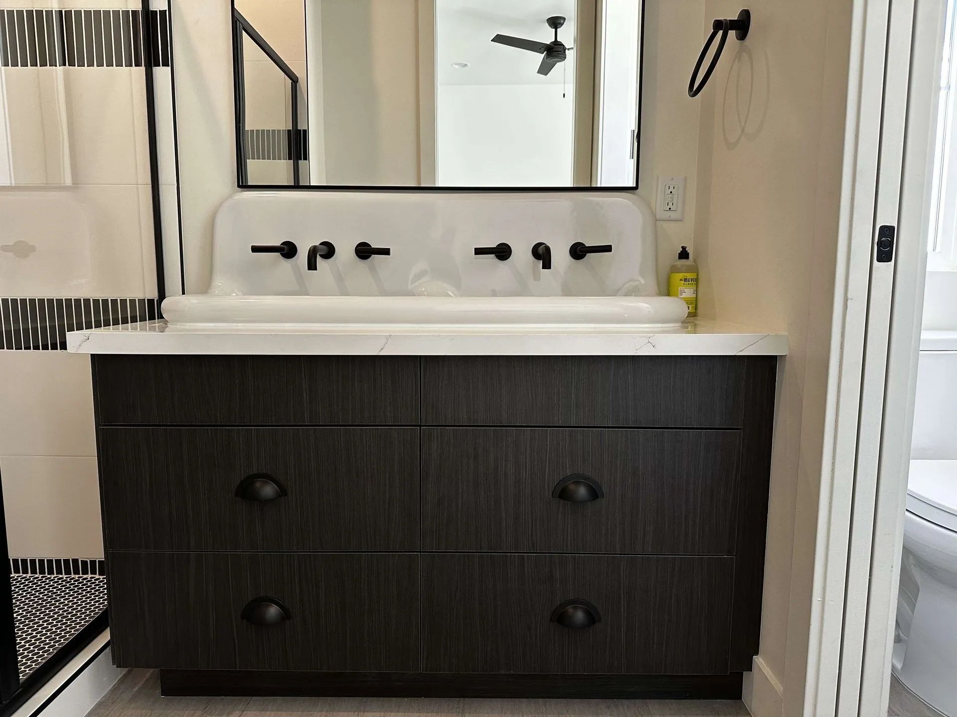 Bathroom vanity with dark wood drawers, a white sink, and black faucets.