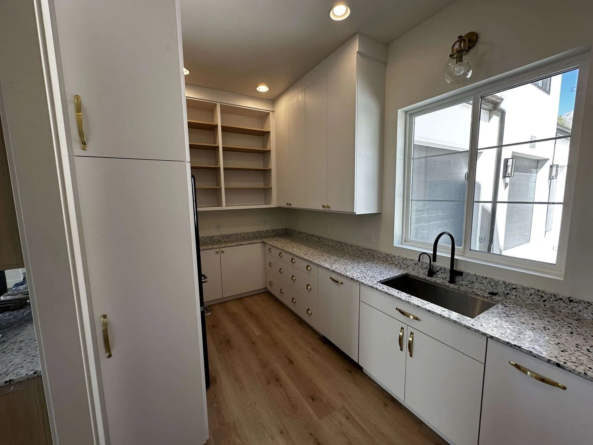 White kitchen with granite countertops, stainless steel sink, and wood flooring.