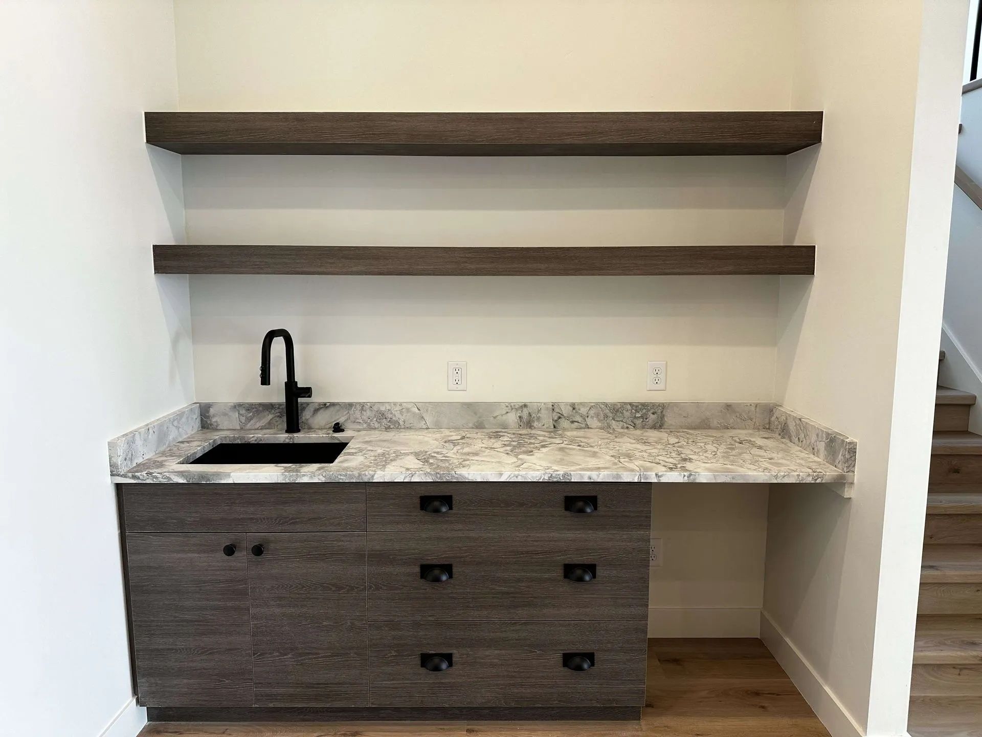 Built-in bar with gray cabinetry, a black sink, and floating shelves. Granite countertop.