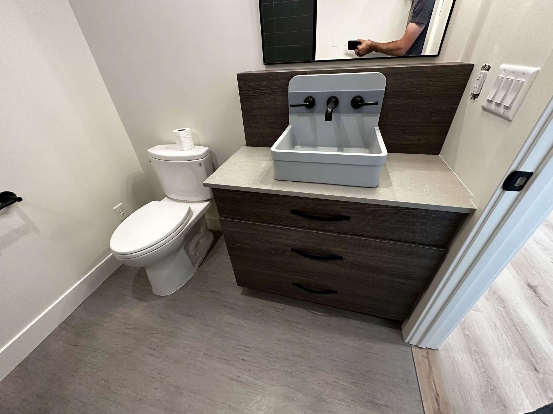 Bathroom with toilet, sink, and dark wood vanity; gray floor and white walls.