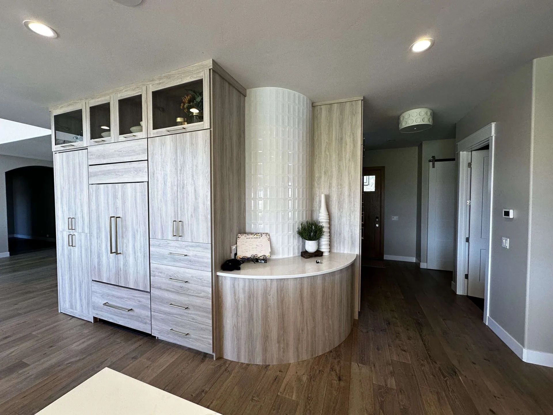 Modern kitchen with light wood cabinetry, built-in refrigerator, and curved countertop.