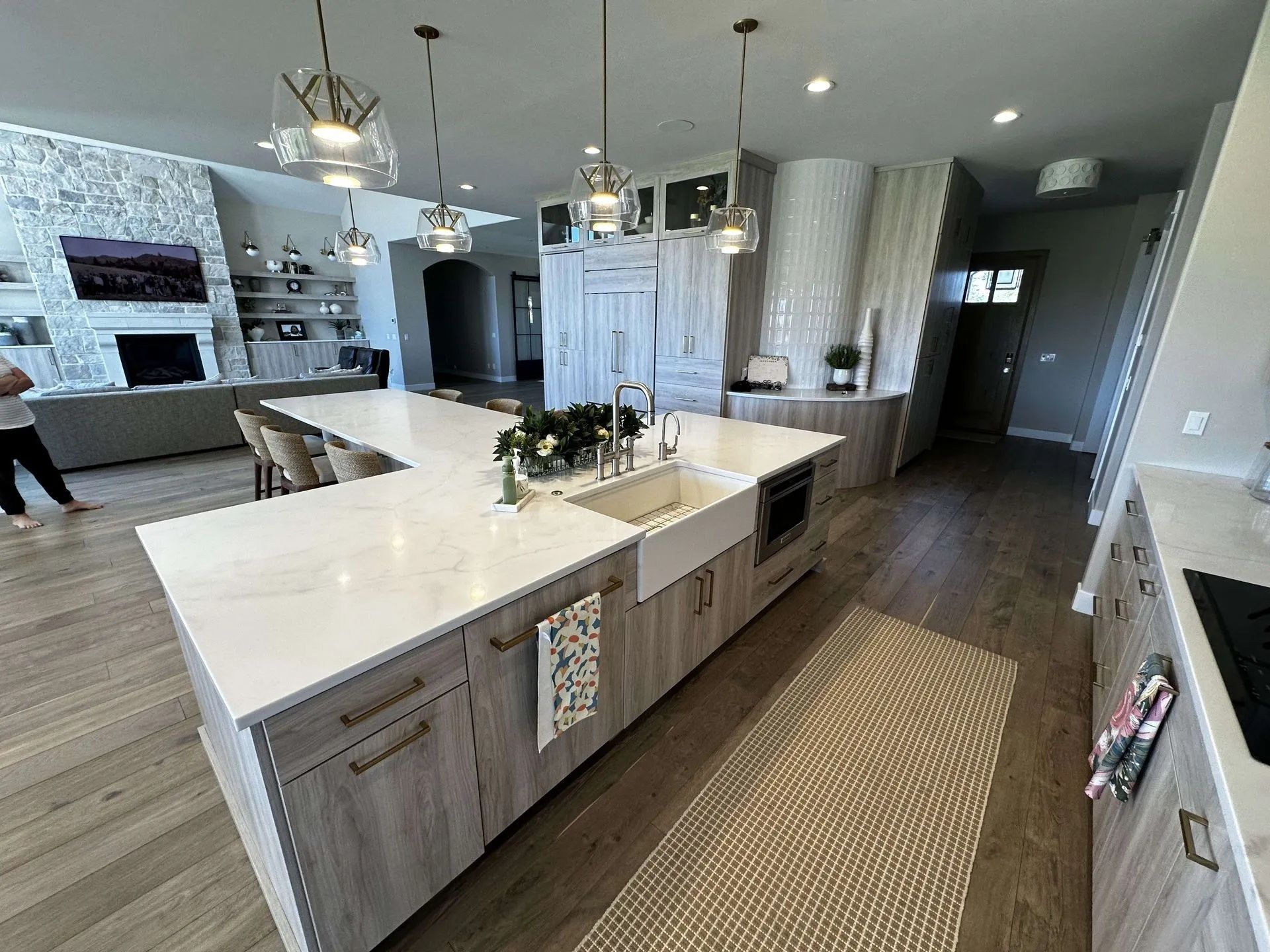 Modern kitchen with large island, farmhouse sink, light wood cabinets, and pendant lights.