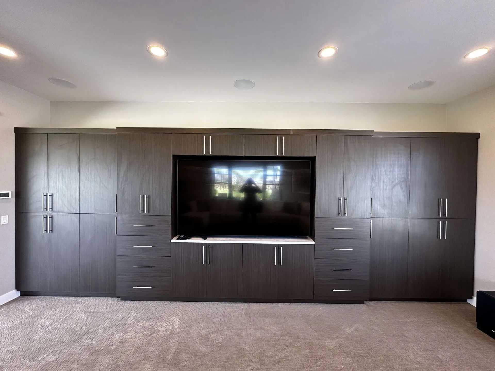 Dark wood entertainment center with TV, drawers, and cabinets in a room with recessed lighting and carpet.