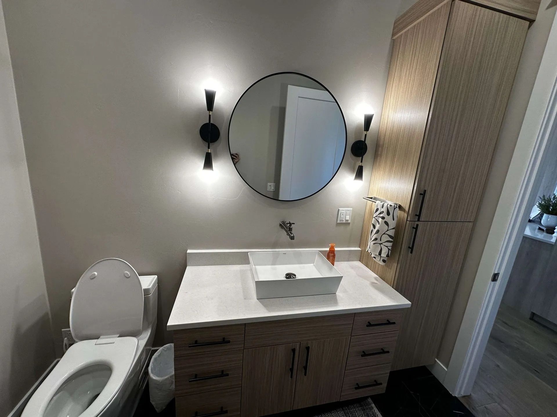 Bathroom with a round mirror, modern lighting, a vessel sink, and a wooden cabinet.