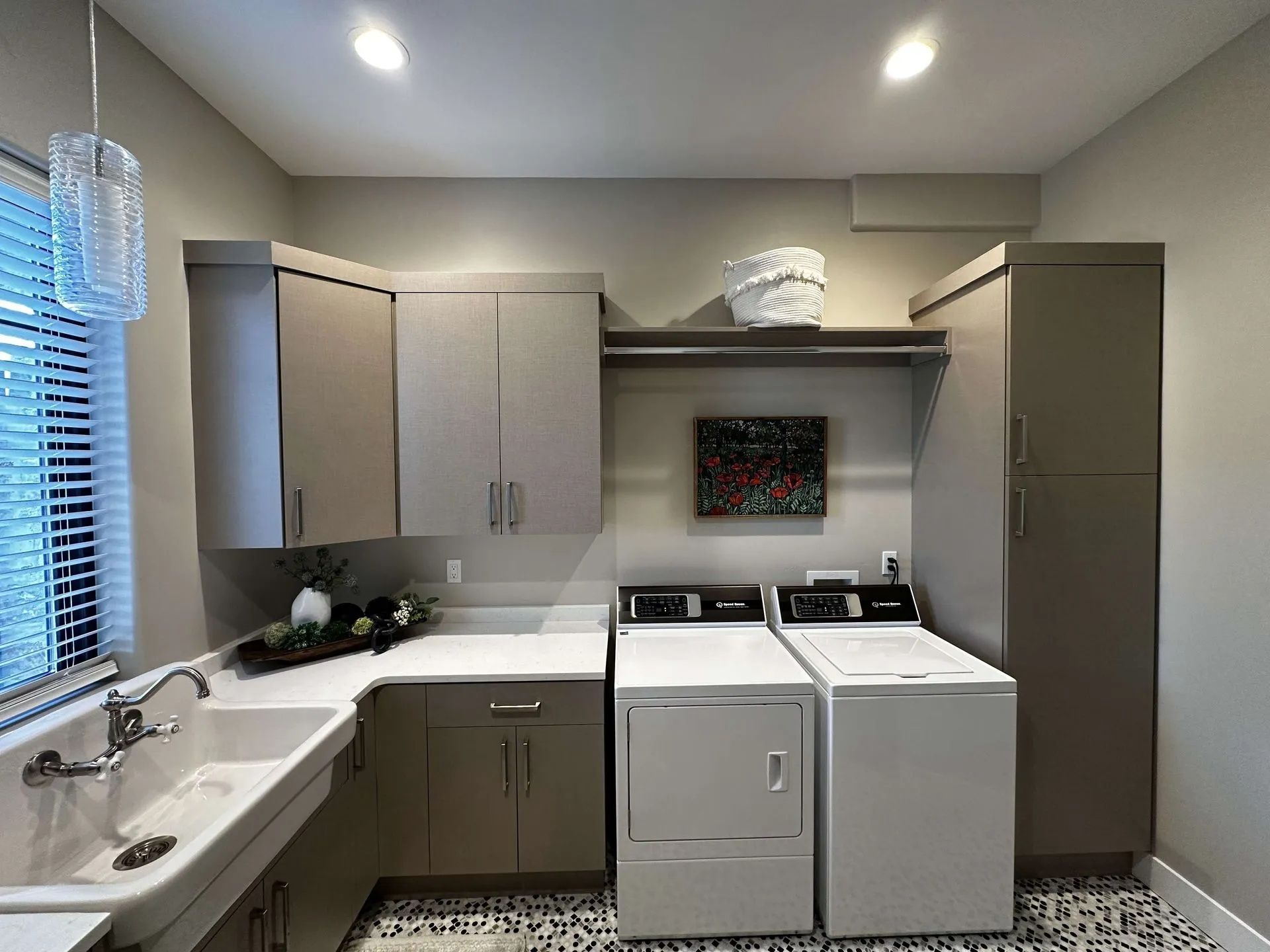 A laundry room with neutral cabinets, a sink, and a washer/dryer set.