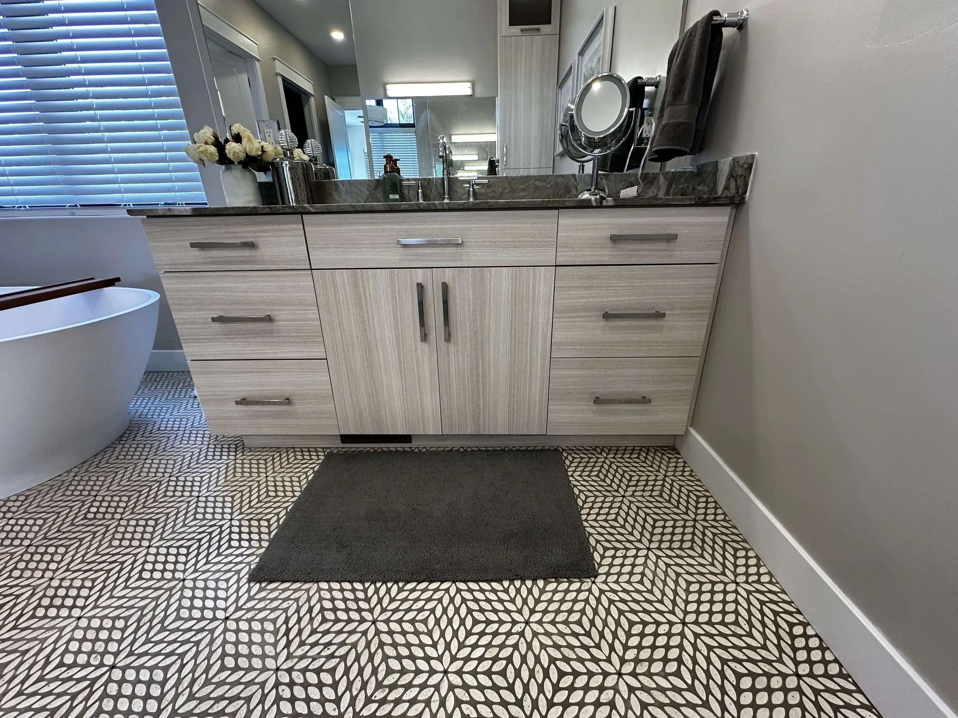 Bathroom with a vanity and patterned floor. The vanity has drawers, a countertop, and a mirror. A bathtub is in the background.